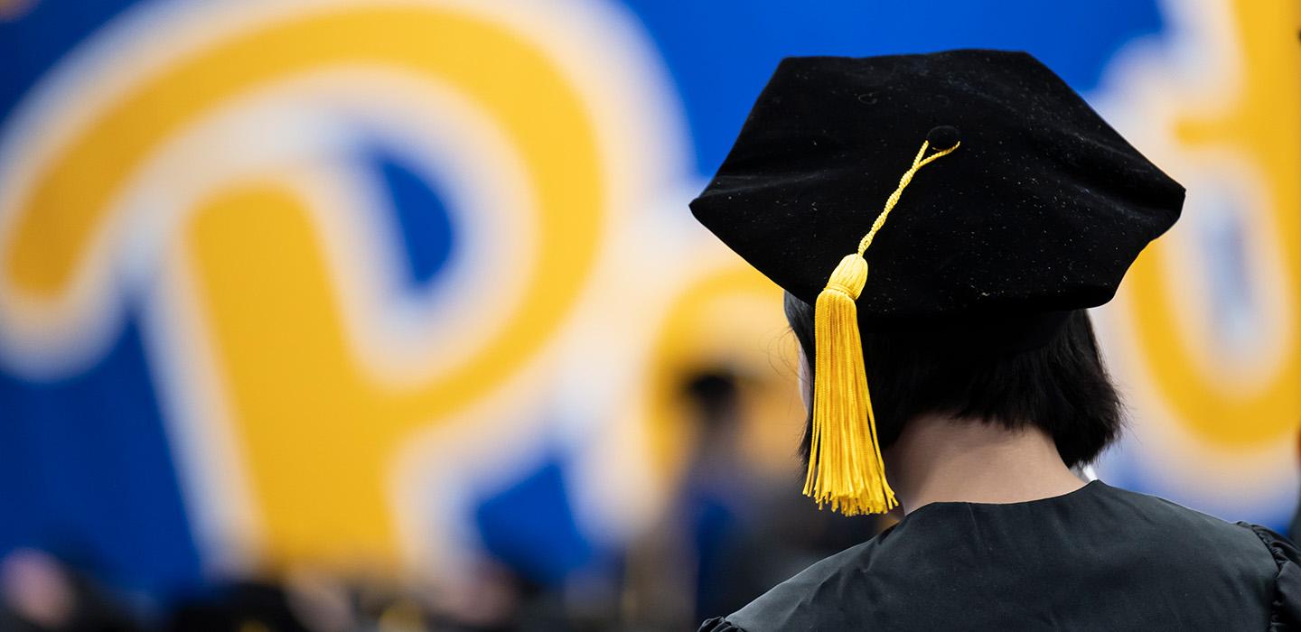 A person stands facing away, with a black velvet tam with a yellow cord on their head