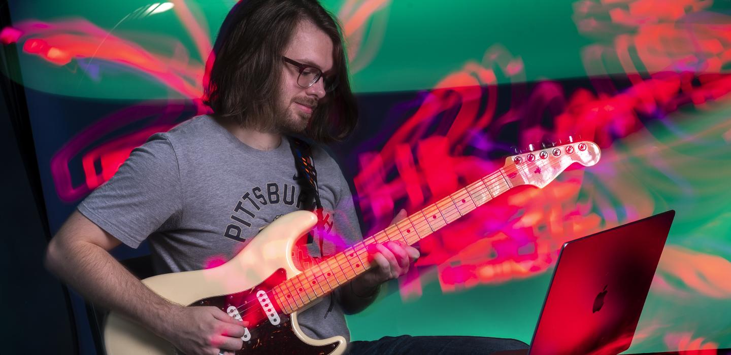 A person looks at a laptop while playing guitar surrounded by neon illustrations