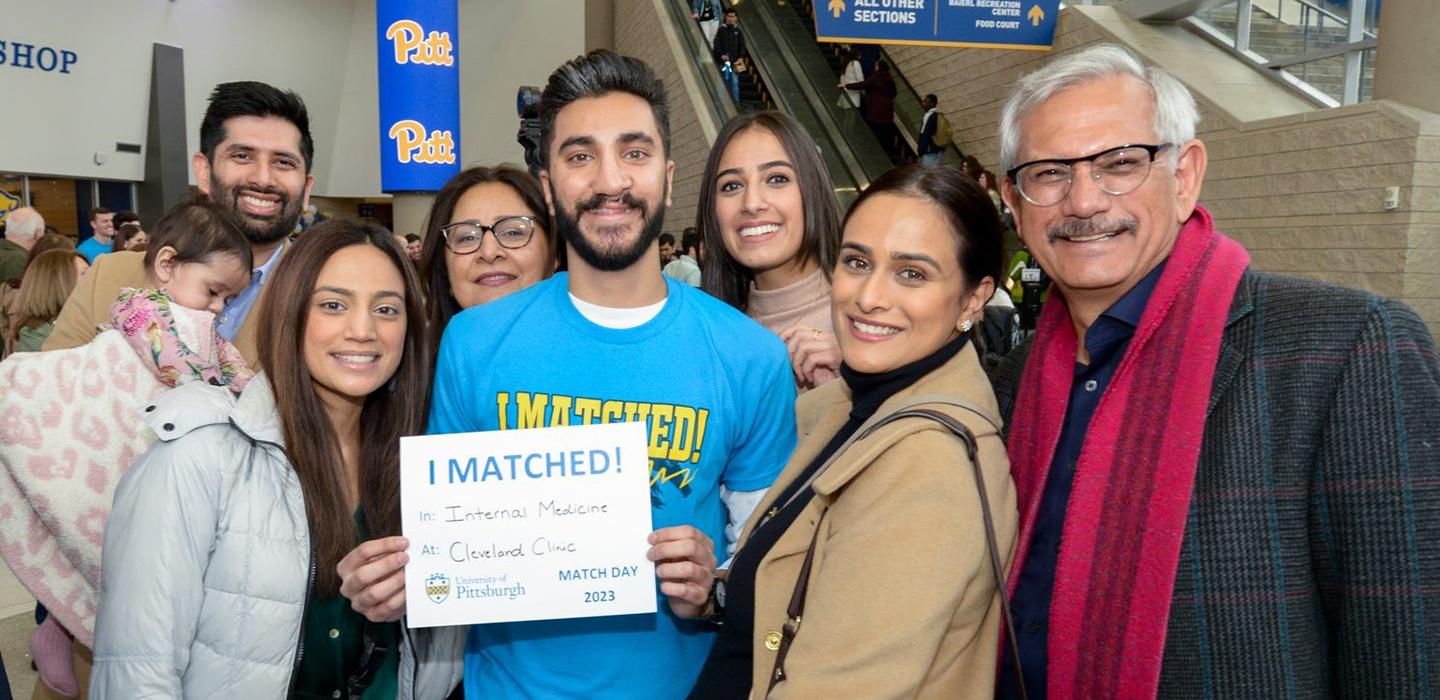 A person in a blue shirt surrounded by family members holds up a sheet of paper that reads I matched