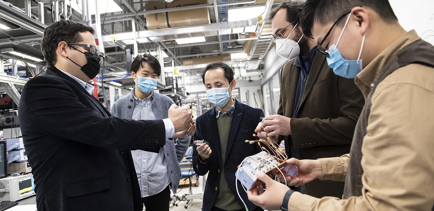 People stand around computing equipment in face masks