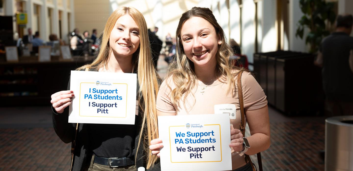 two people holding "We support PA students, we support Pitt" signs