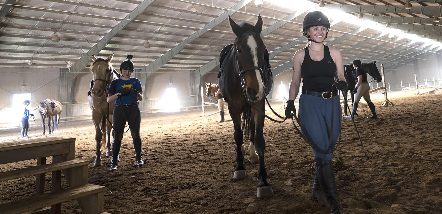 Girls lead horses across the inside of a barn