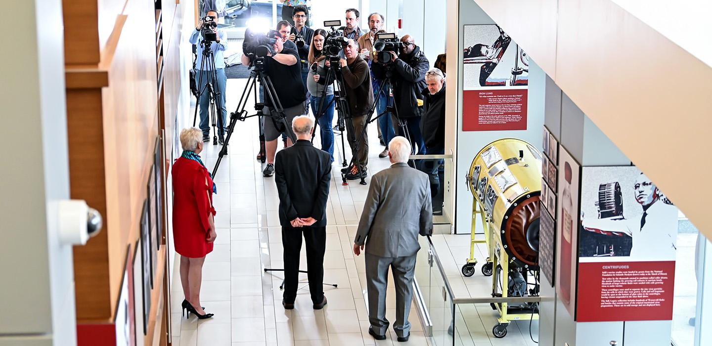 Reporters and cameras stand at the entrance of an exhibit