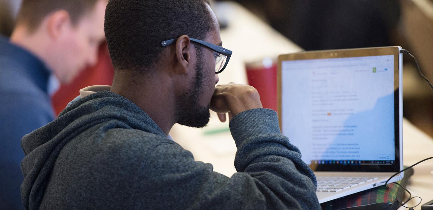 A person in a black hoodie looks at a laptop screen