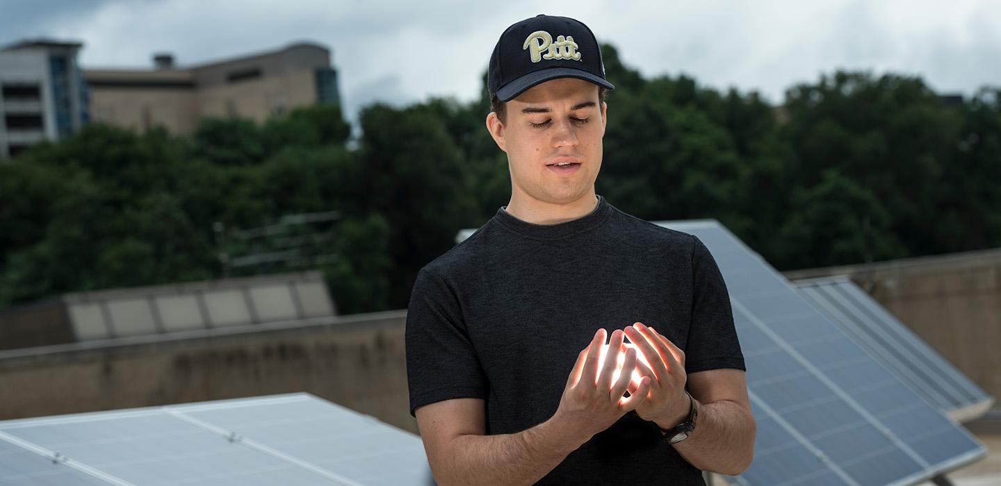 Senior Sam Ressin standing in front of an array of solar panels, with a glowing object in his hands