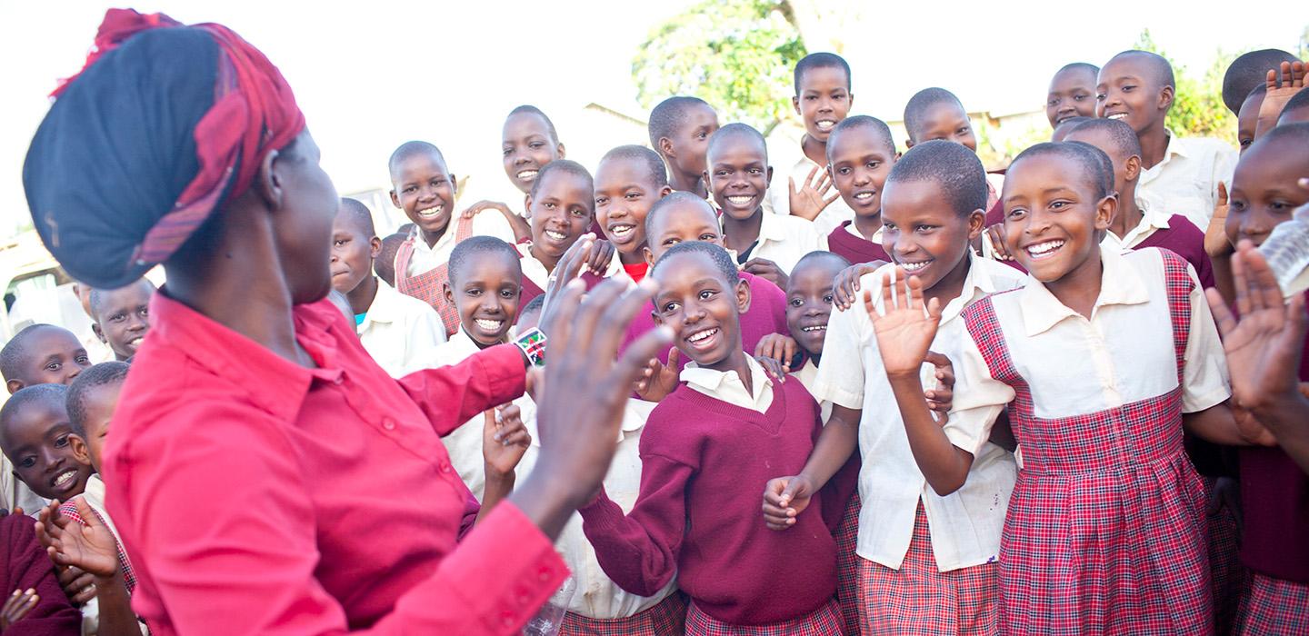 Children in red school outfits dance with a woman in a red collared shirt