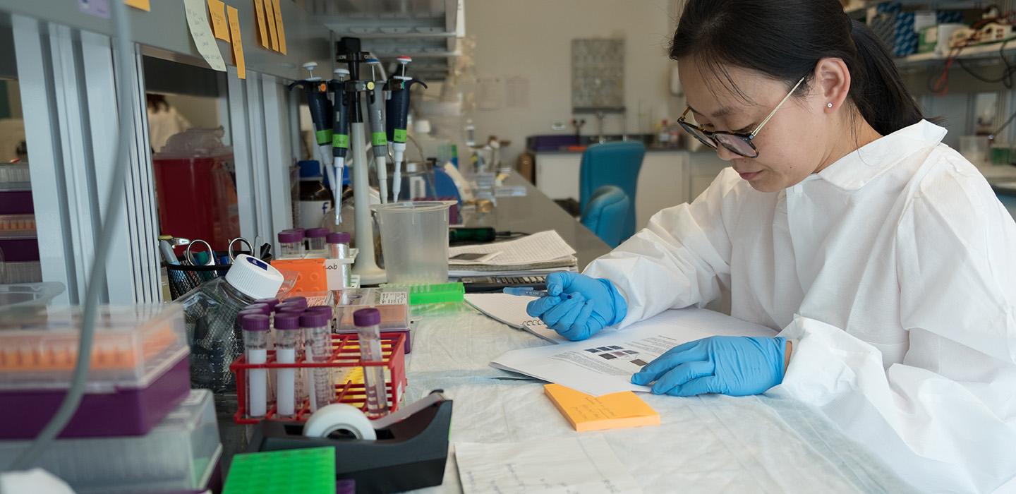 A researcher in gloves and a lab coat takes notes in the Aging Institute laboratory