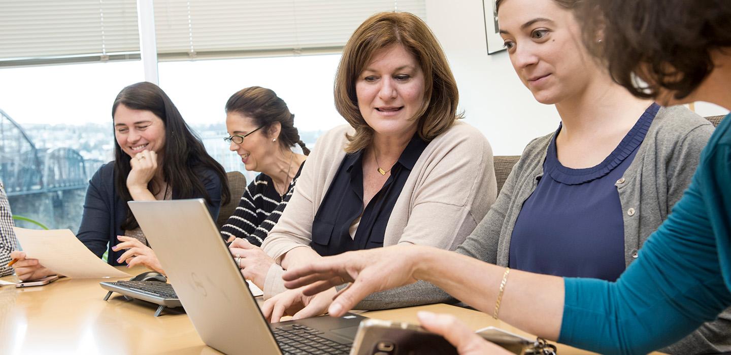Faculty members share a laptop at a table