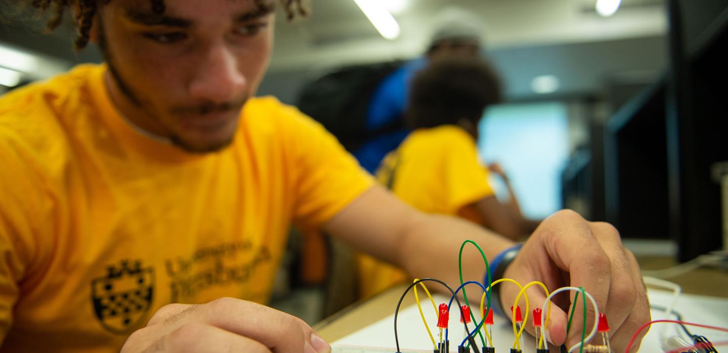 a student in a yellow Pitt shirt working with wires