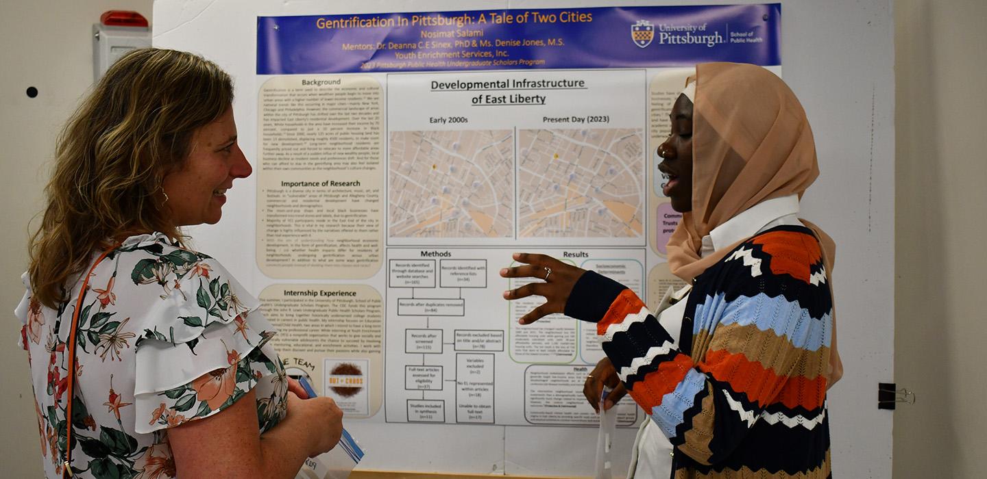 A student talks to a person about their research in front of a poster