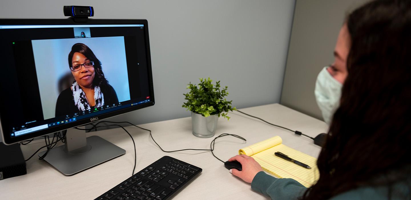 A person wearing a face mask talks to a therapist on a video call
