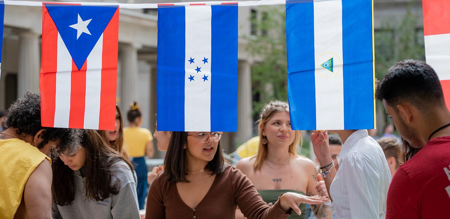 People talk and eat behind flags of Latin American countries hanging in the foreground