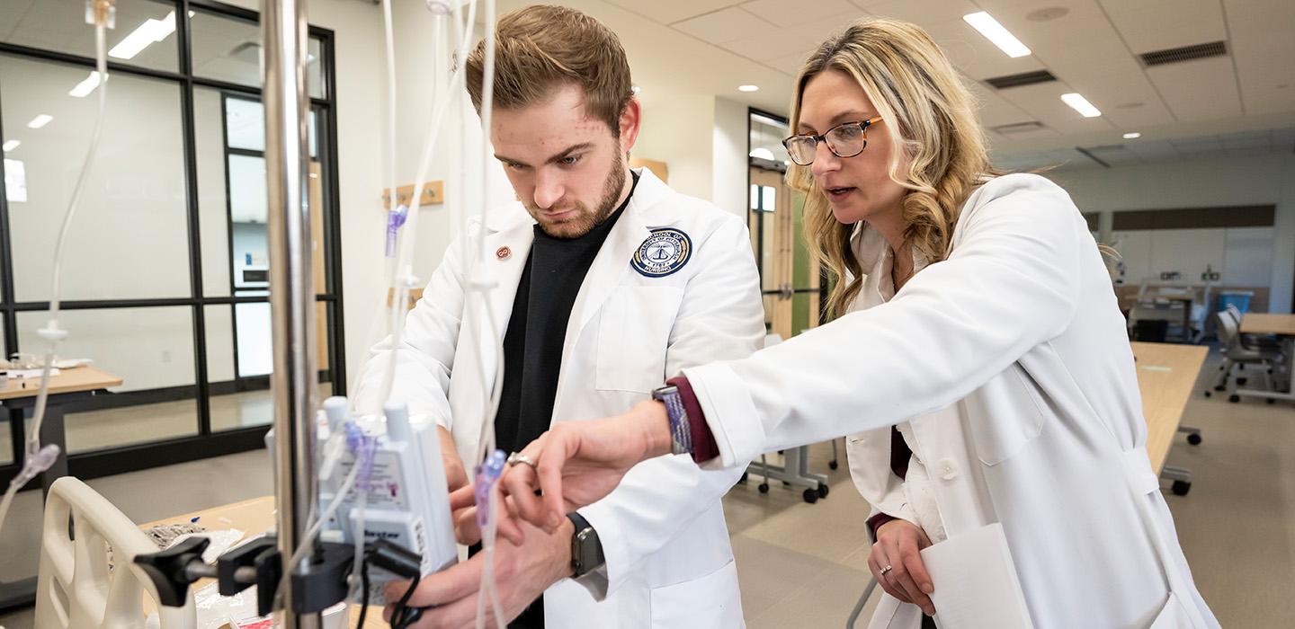 Two nurses in white coats work on an IV stand
