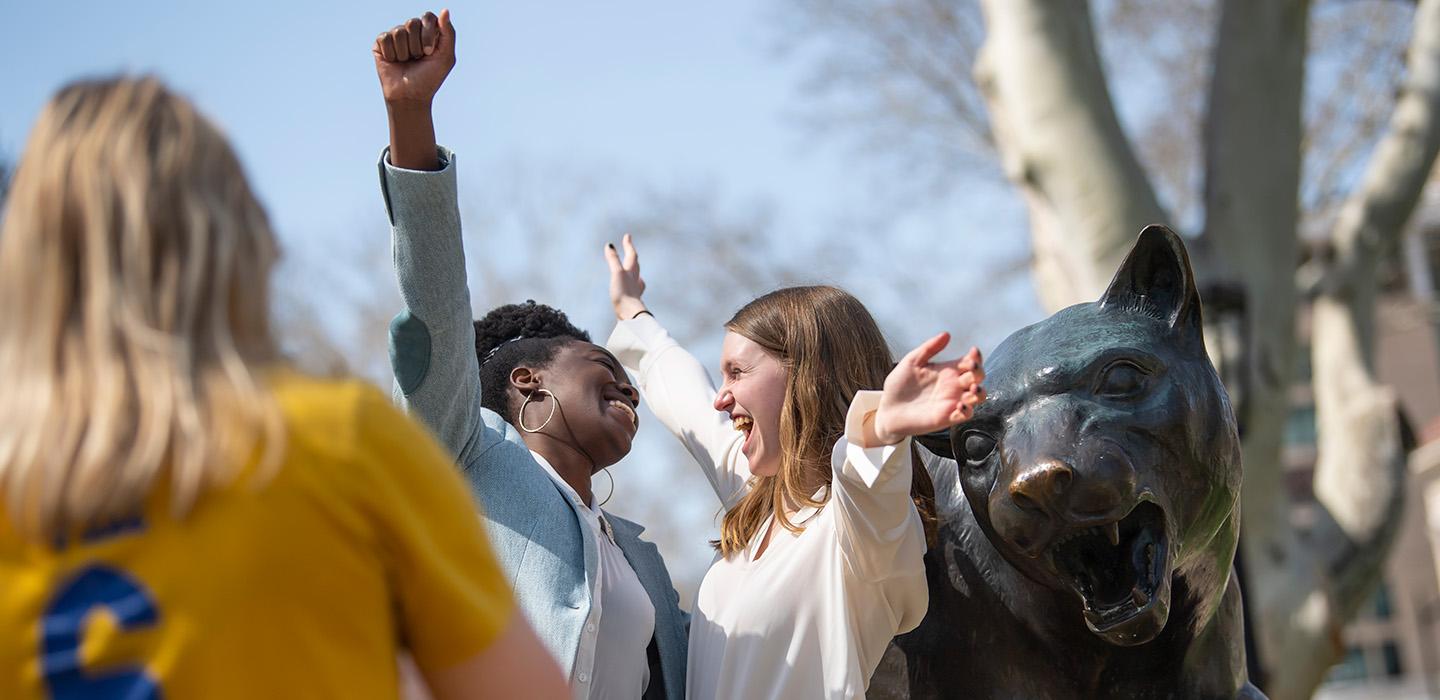 Two students hug next to a Panther statue