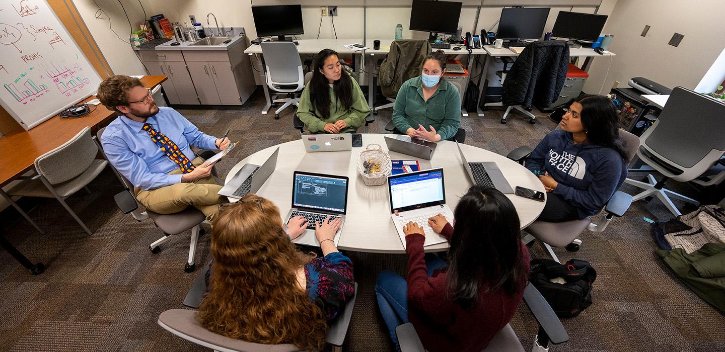 Six people sit around a table with laptops