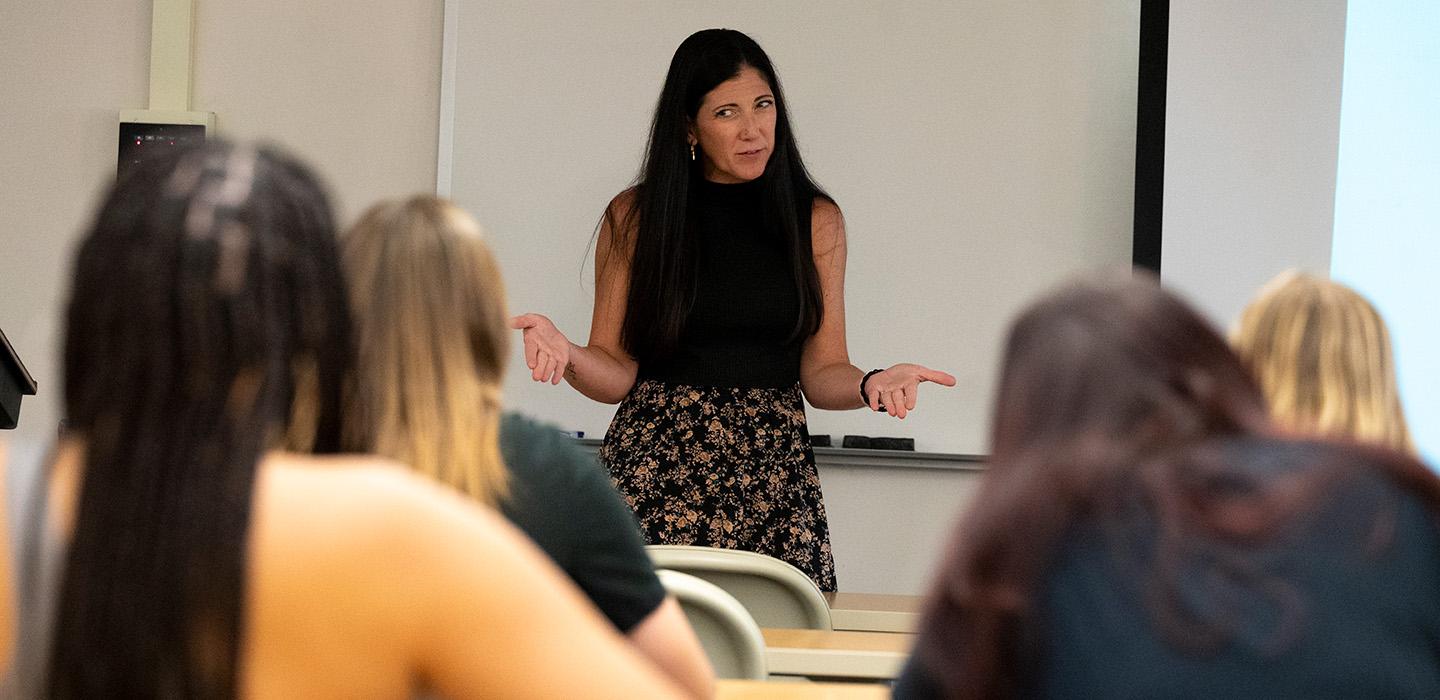 A professor gestures in front of students sitting in rows of desks