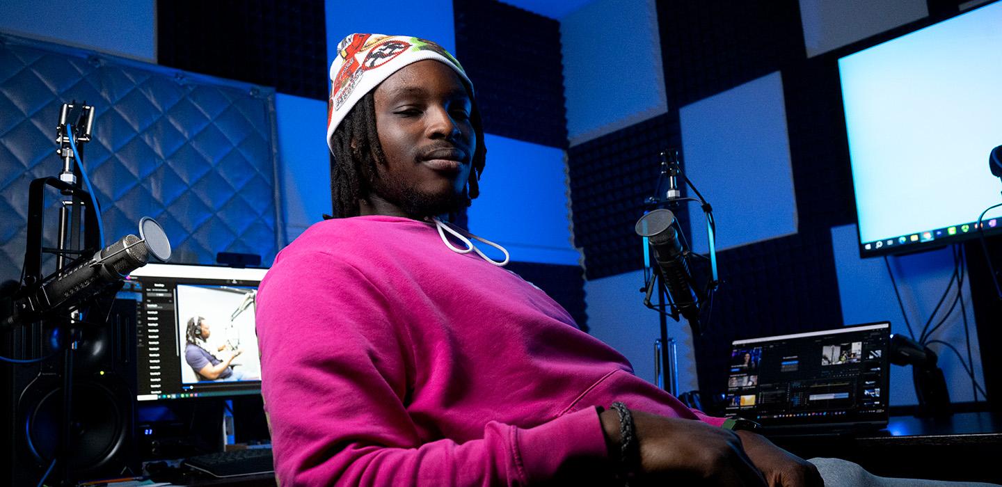 Kehinde sits in a podcast studio, surrounded by microphones and computer monitors