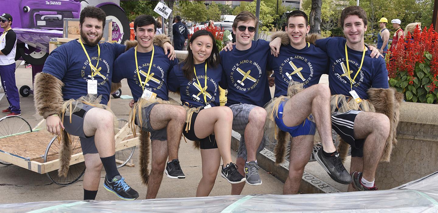 A group of students poses with their legs raised in the air