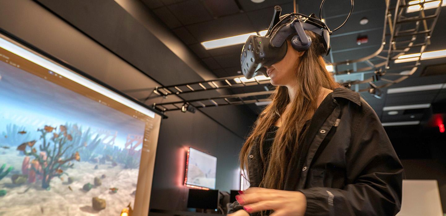 Synychych wears a VR headset to test her scuba diving application, displayed on a projector screen