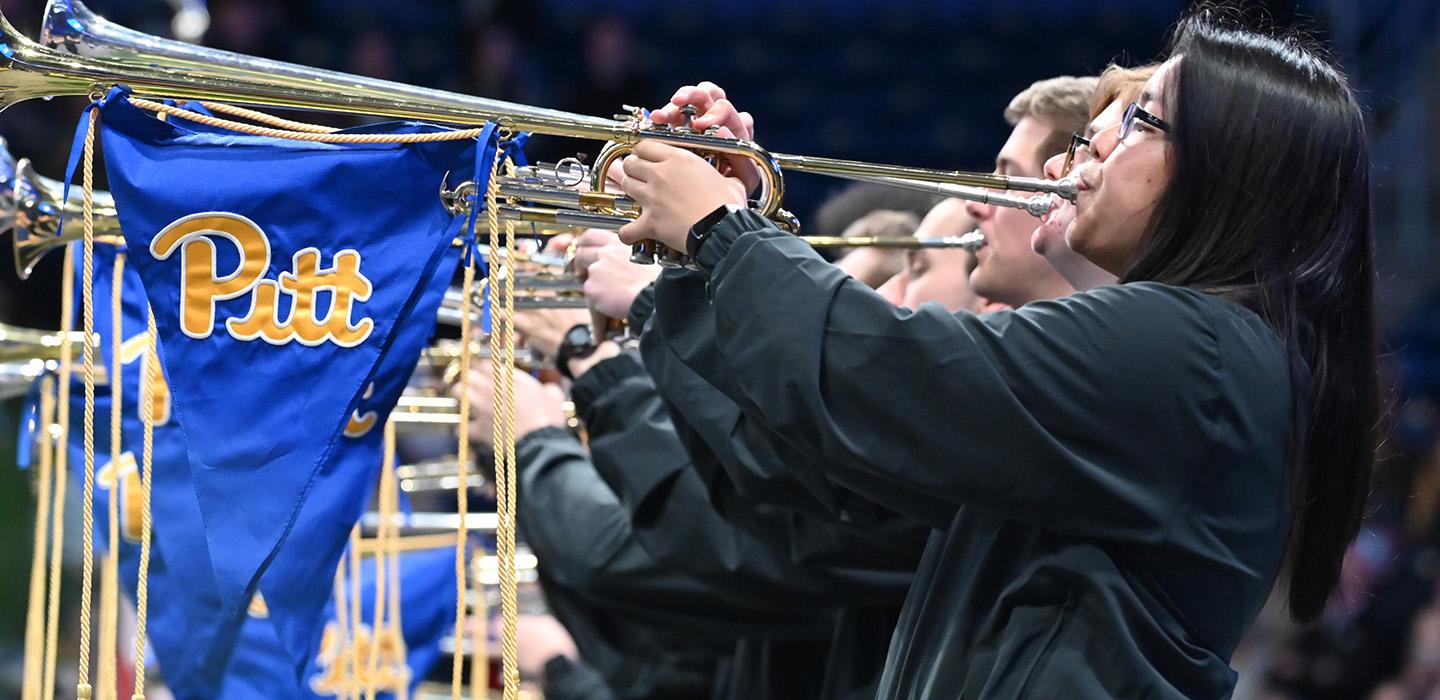 A line of people play horns with Pitt flags