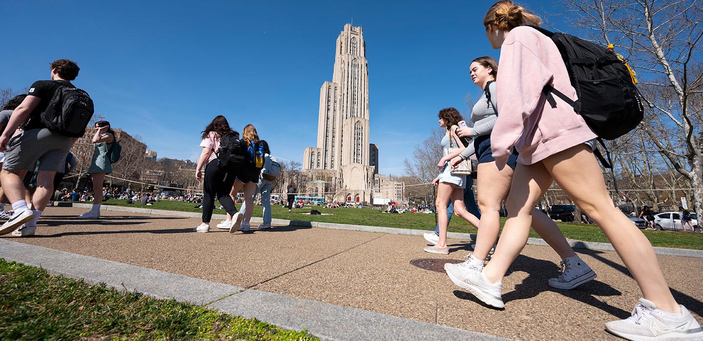 Groups of students walk by Schenley Plaza, with the Cathedral of Learning in the background