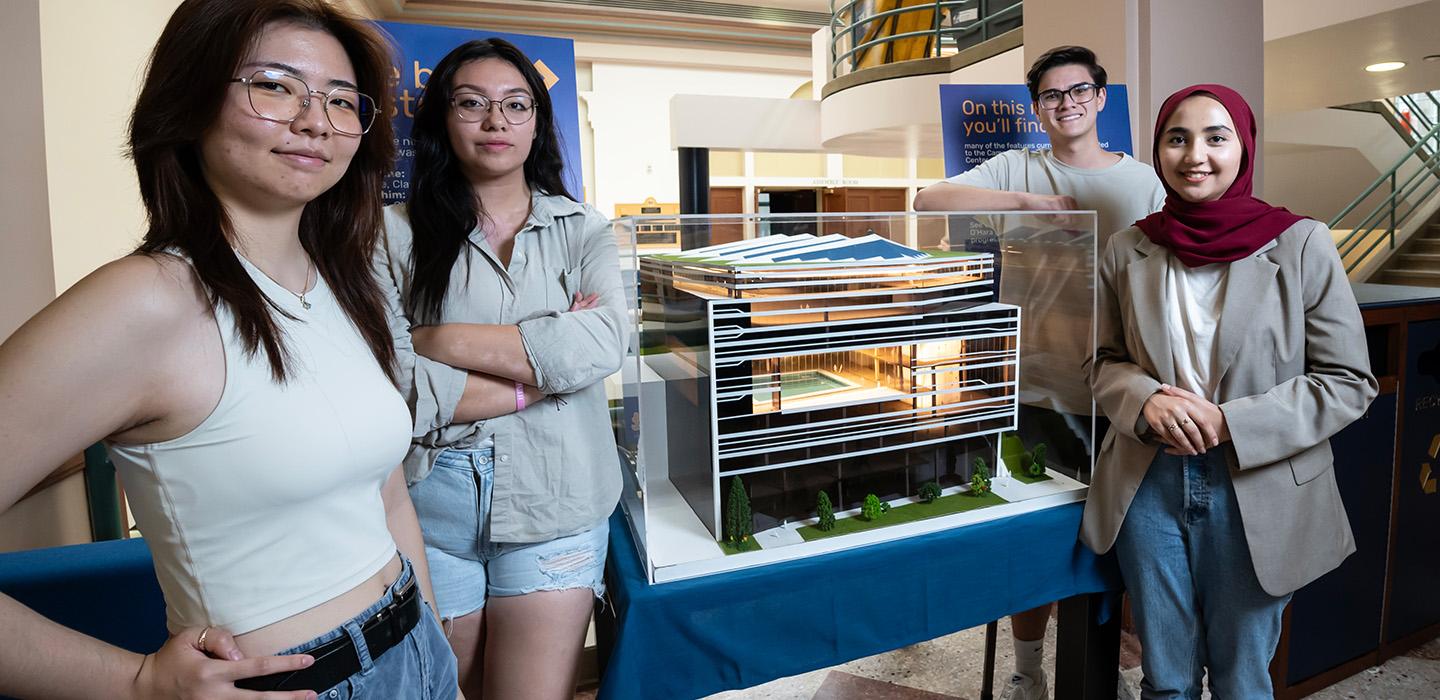 Four students stand around their model behind glass