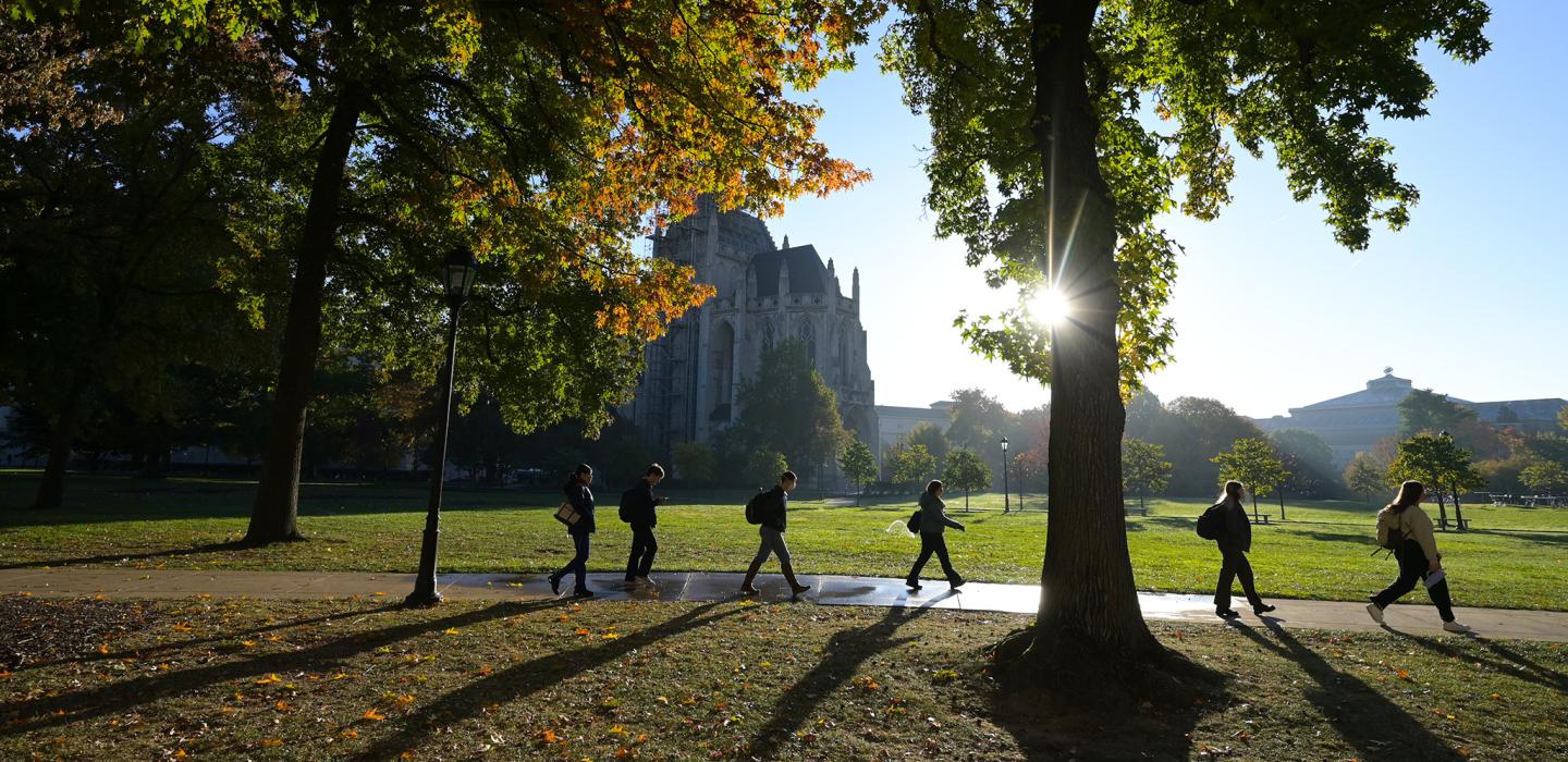 Students walk on the sidewalk of the Cathedral lawn, with Heinz Chapel visible in the background, during the fall.