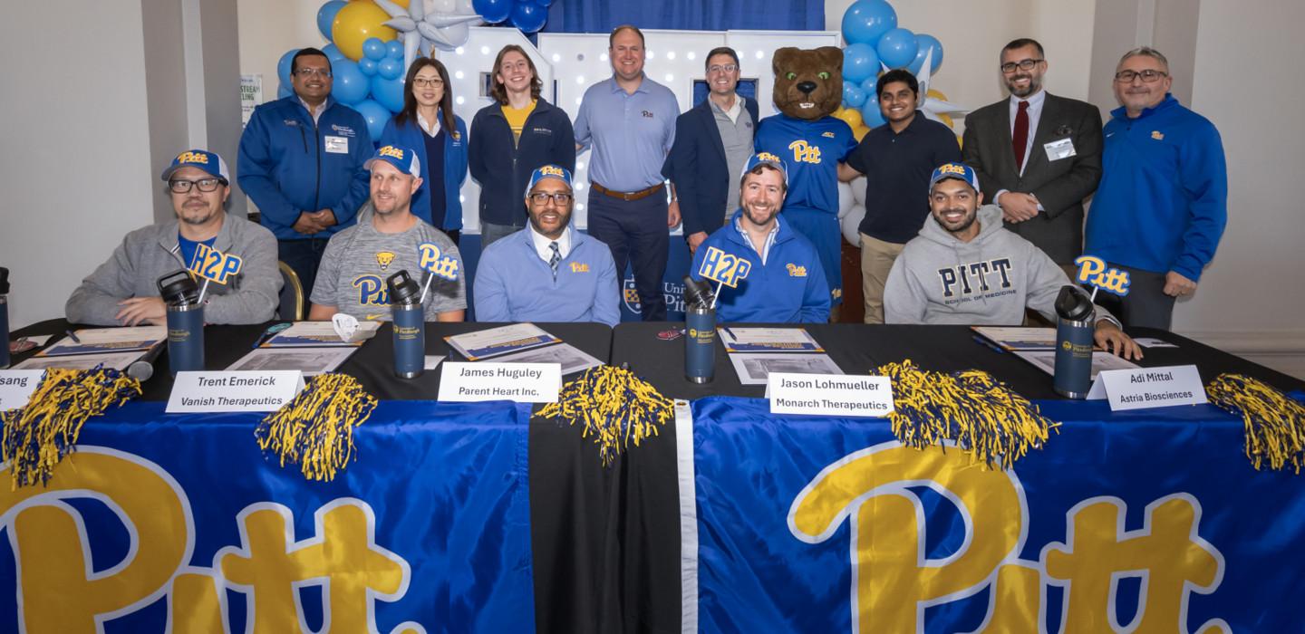 Pitt startup founders pose at a table with Pitt banners and Roc the panther