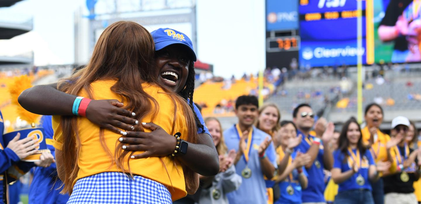 Students embrace on the field of the Acrisure Stadium during a Homecoming Football game.