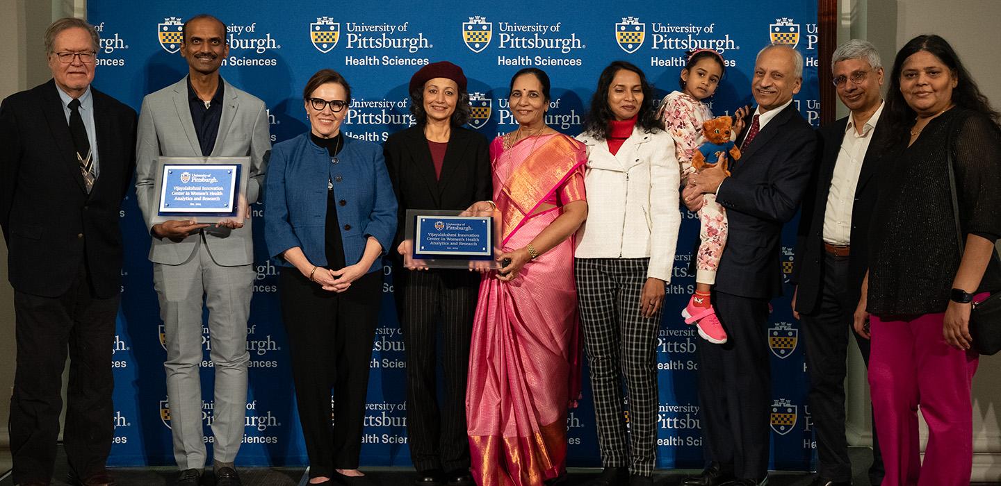 People stand in front of a Pitt health sciences backdrop