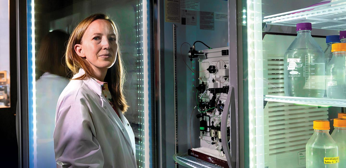 Leah Byrne stands beside a machine and liquid samples in a lab