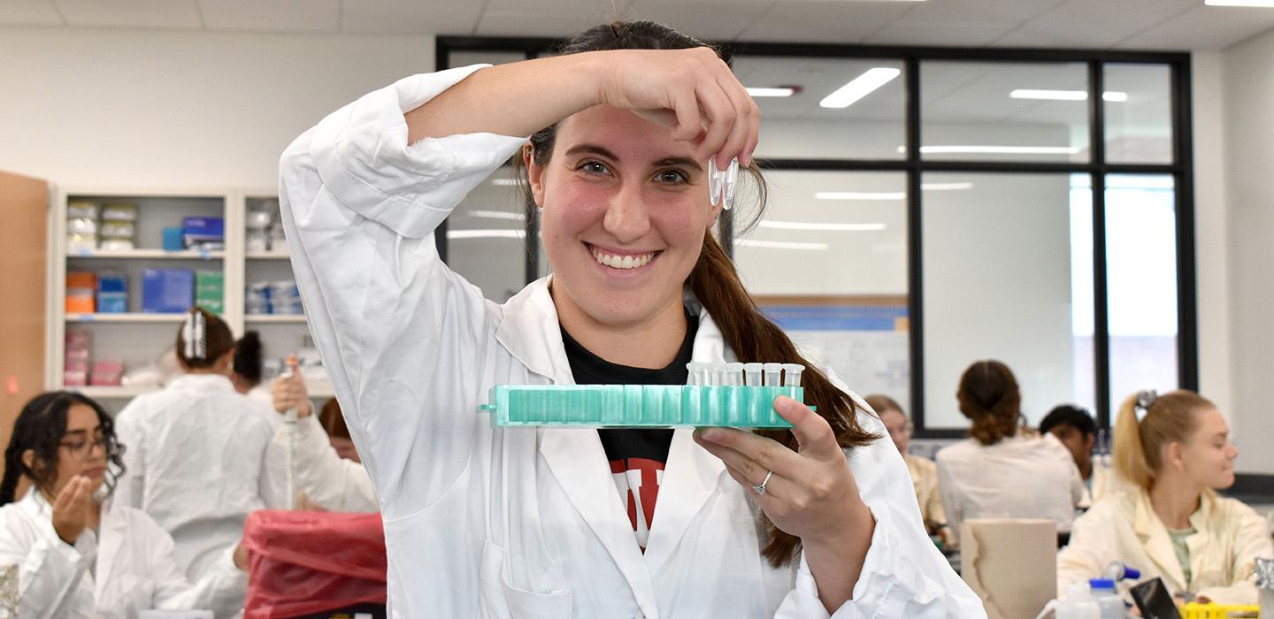 A student in a lab coat holds up a tray of plastic tubes