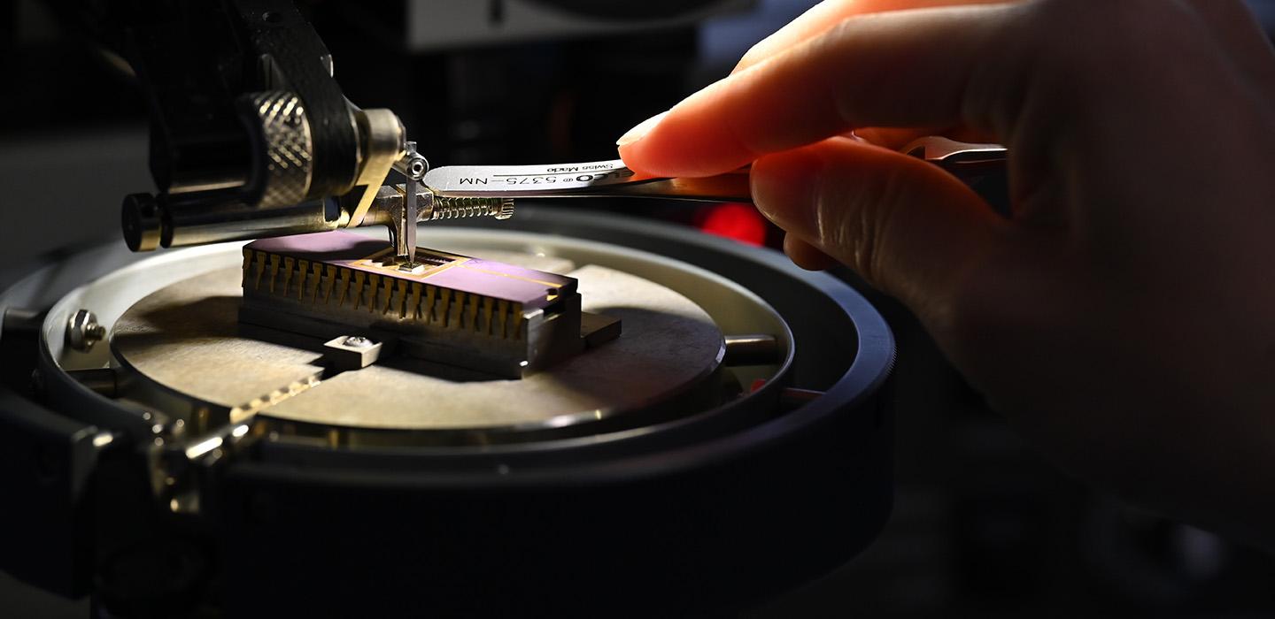A hand uses a tool to adjust a small device