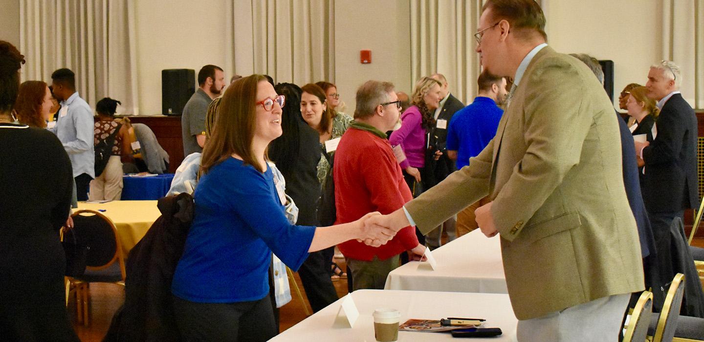 A woman and man shaking hands over a table at an event.
