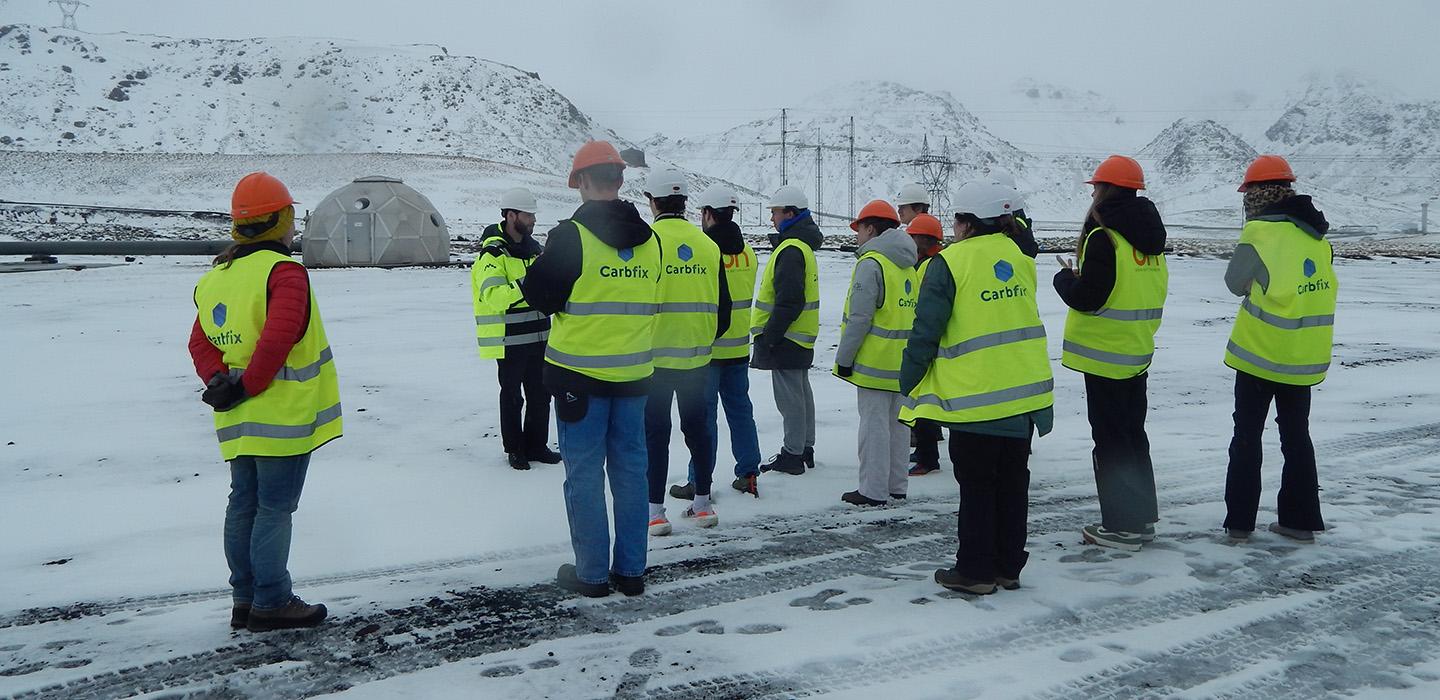 A group of students stand in florescent vests on a snowy plain.