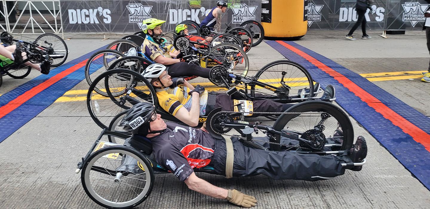 Hand cyclists line up in a row at the marathon starting line.