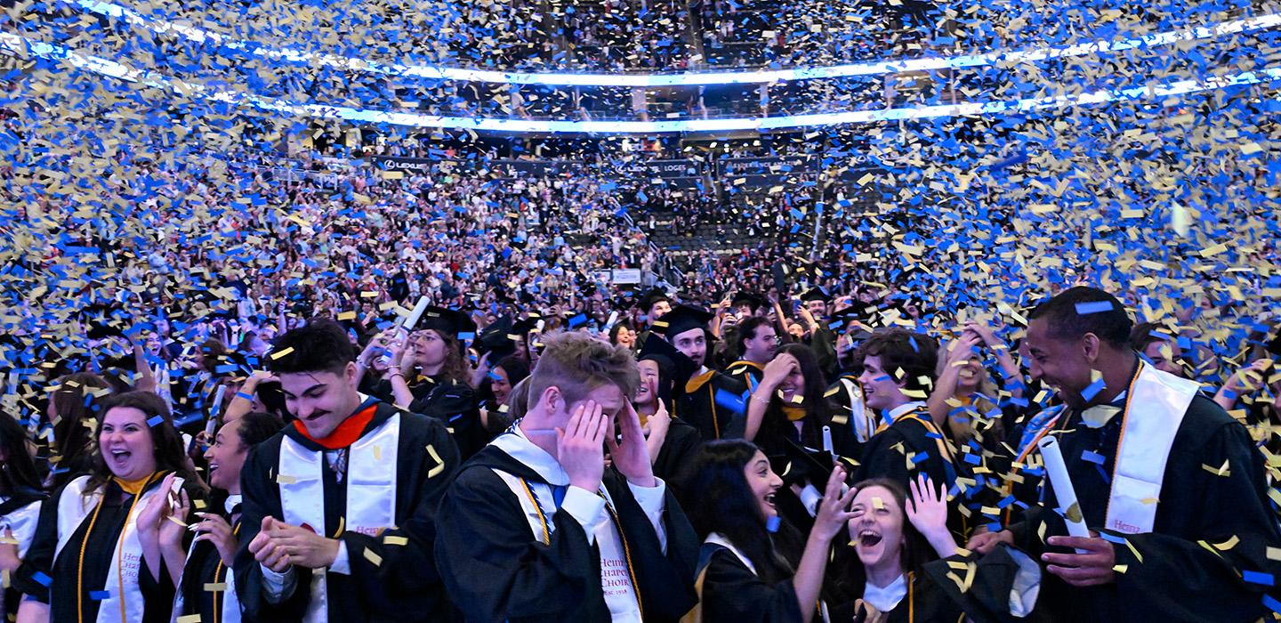 Students at graduation cheering as blue and gold confetti falls