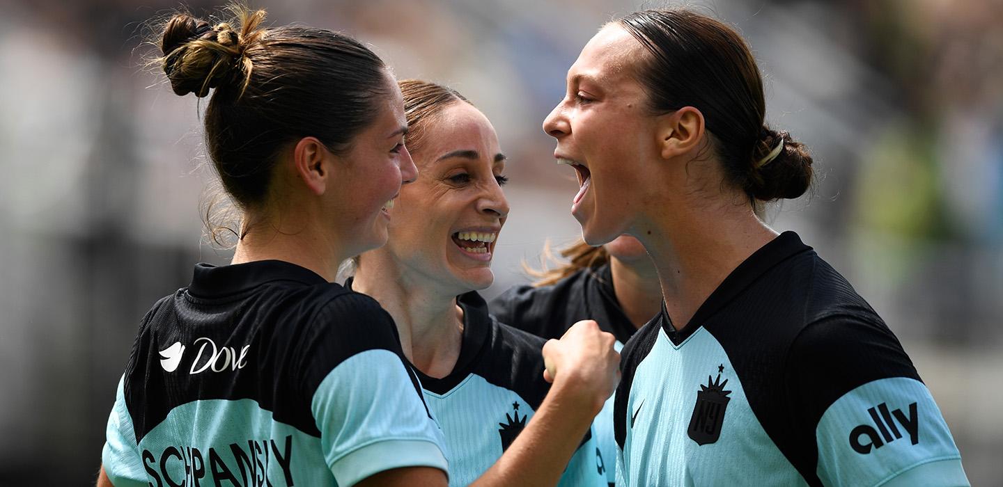 Three soccer players hug and cheer.
