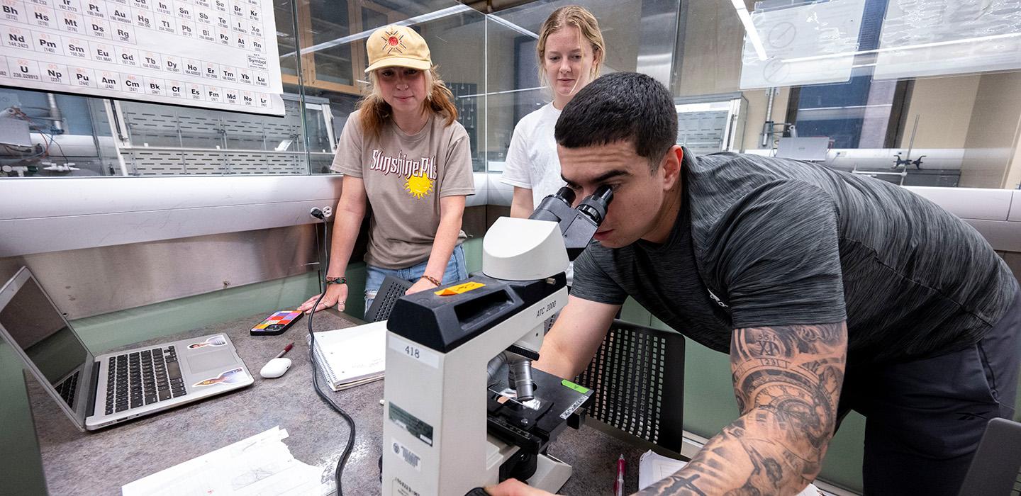 TA Ed Strimlan looks in a microscope while two others watch
