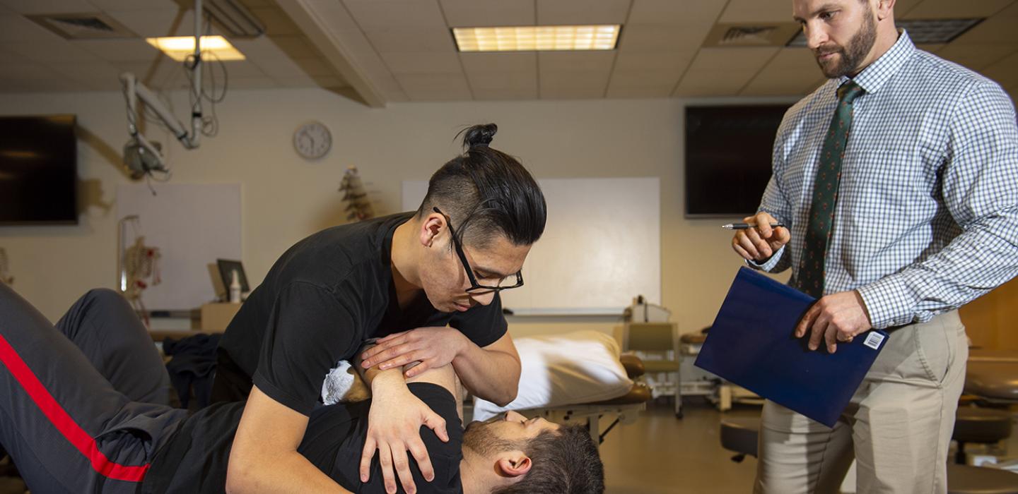 A physical therapy student performs tests on a patient, while a professor observes