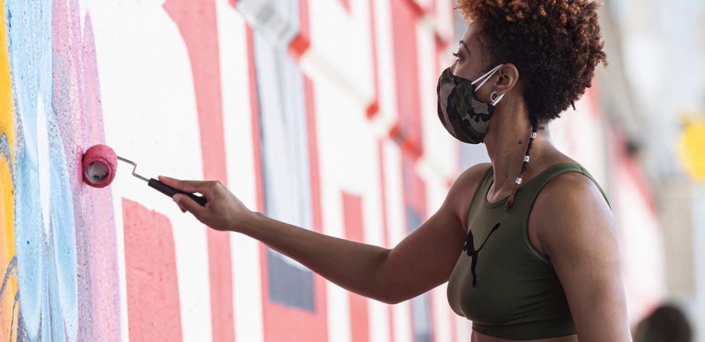 a person in a sports bra paining on a wall with a roller dipped in reddish paint