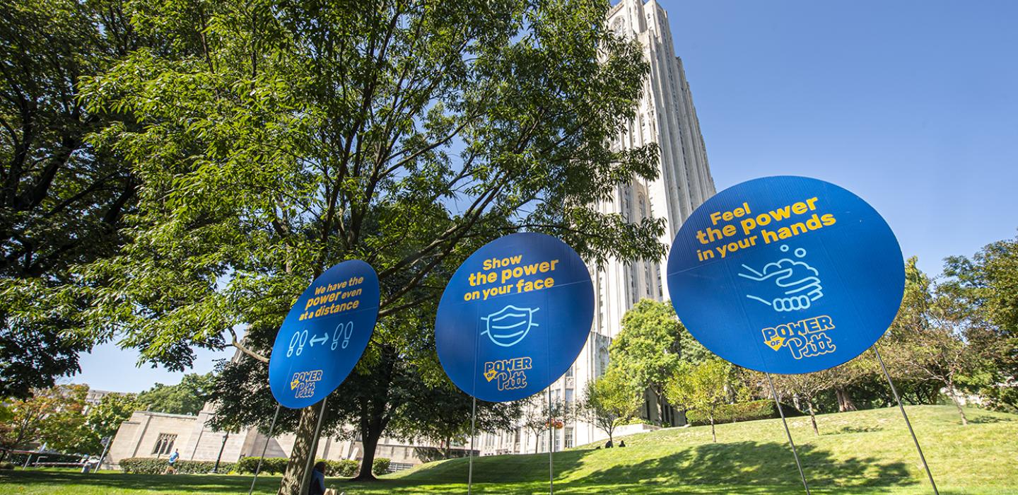 Blue signs on a lawn in front of the Cathedral of Learning