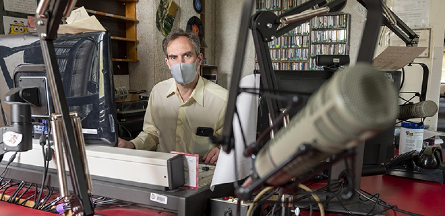 a masked person behind an elaborate set of microphones and dials