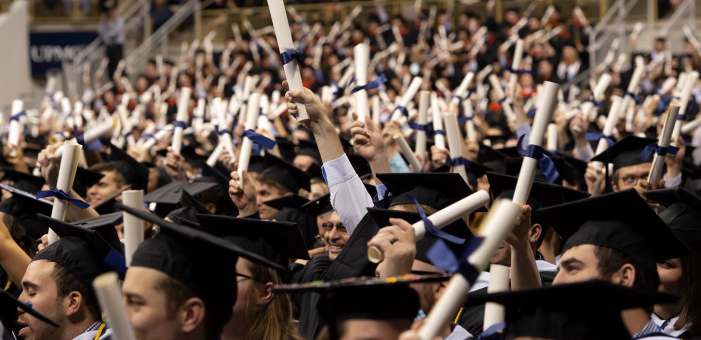 group of students in graduation regalia holding scrolls high in the air