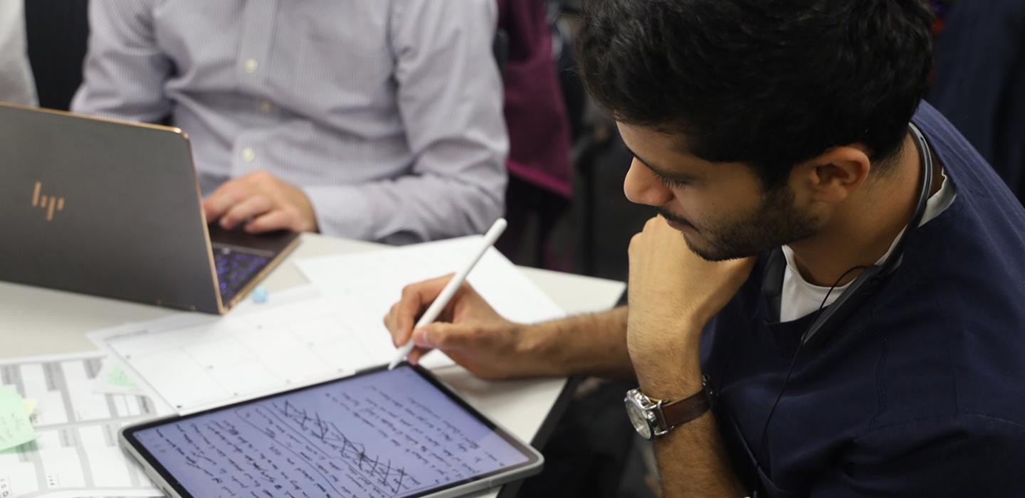 Rana in dark blue scrubs taking notes on an electronic tablet