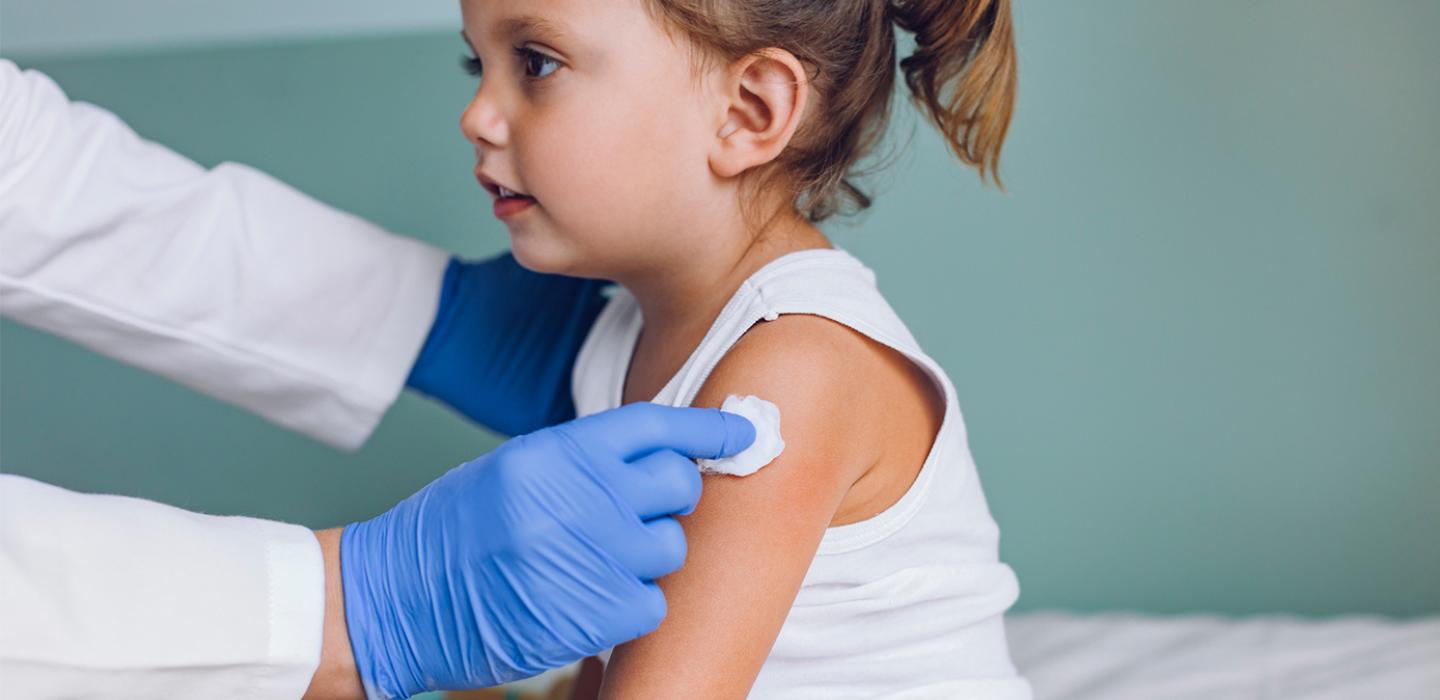 a small child in a white outfit with a gloved hand putting a cotton ball on the child's arm