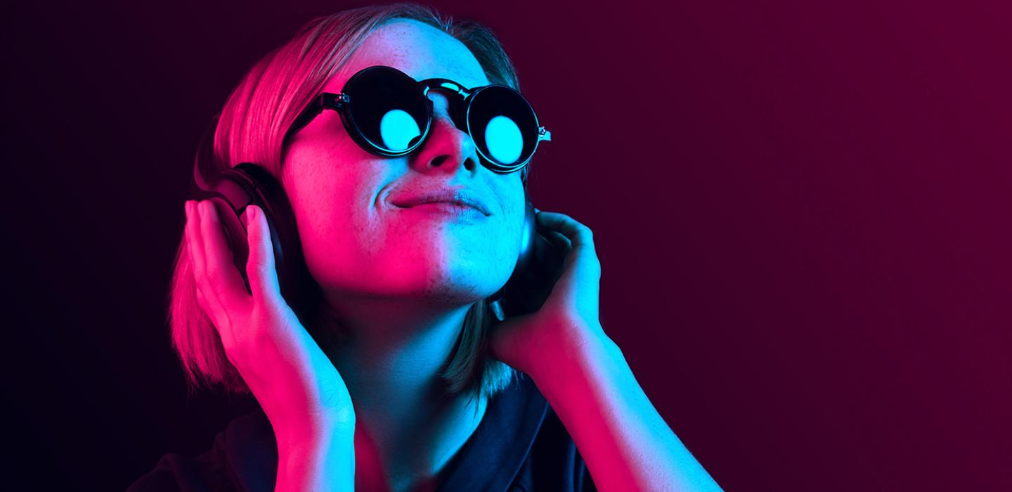 A person in sunglasses listening to music on headphones in a neon pink-blue light