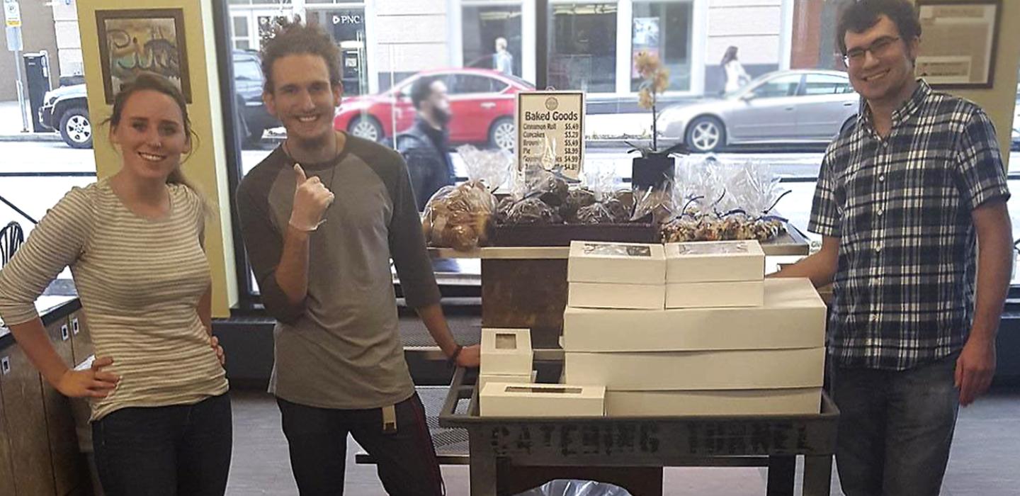 a woman and two men standing in front of white boxes of recovered baked goods