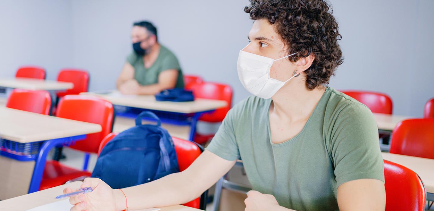 two students sitting socially distant in a classroom, wearing face coverings