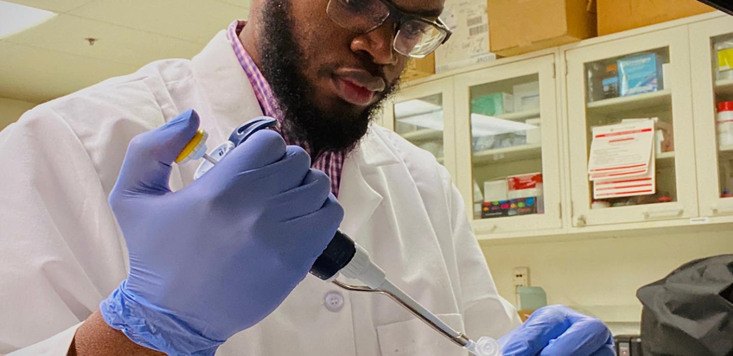 A man in a white coat and gloves works in a lab